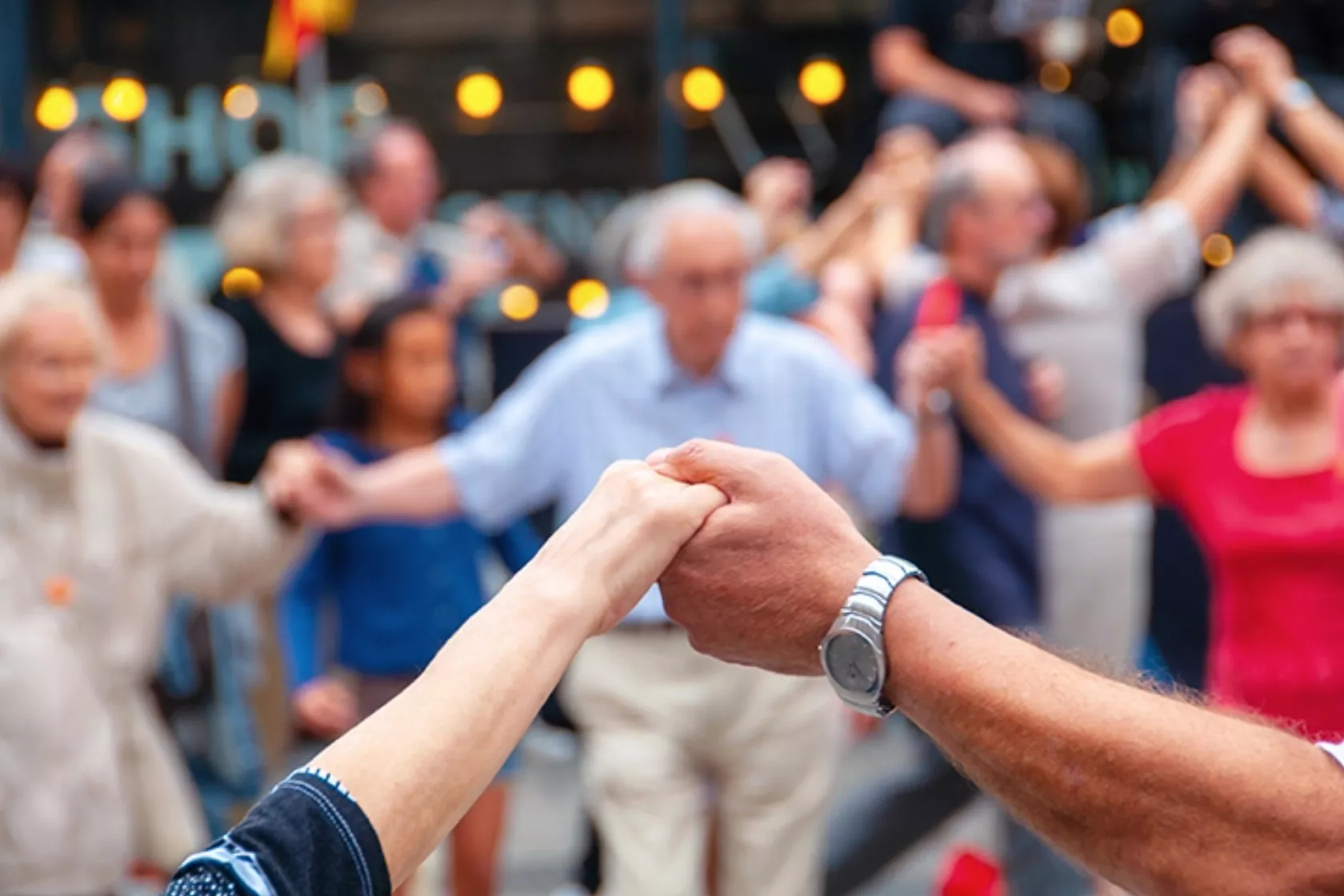 Senioren tanzen auf einem Fest und halten sich an den Händen.