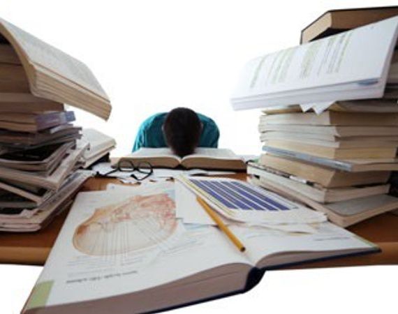 Ein Studierender legt den Kopf auf das Buch, in dem er liest. Neben ihm hohe Bücherstapel.