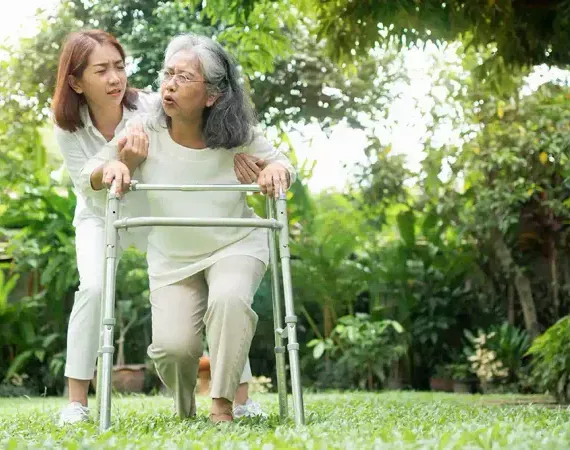 Jüngere Frau stützt eine älter Frau mit einer Gehhilfe in dem Moment, in dem diese stolpert.