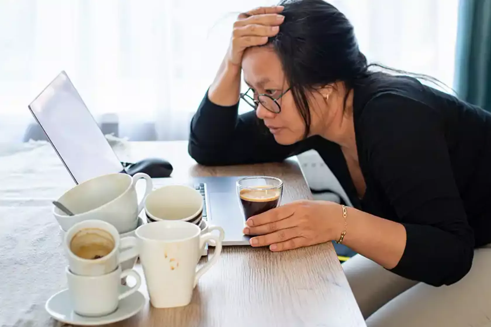 Frau sitzt müde mit vielen leeren Kaffeetassen vor ihrem Computer.