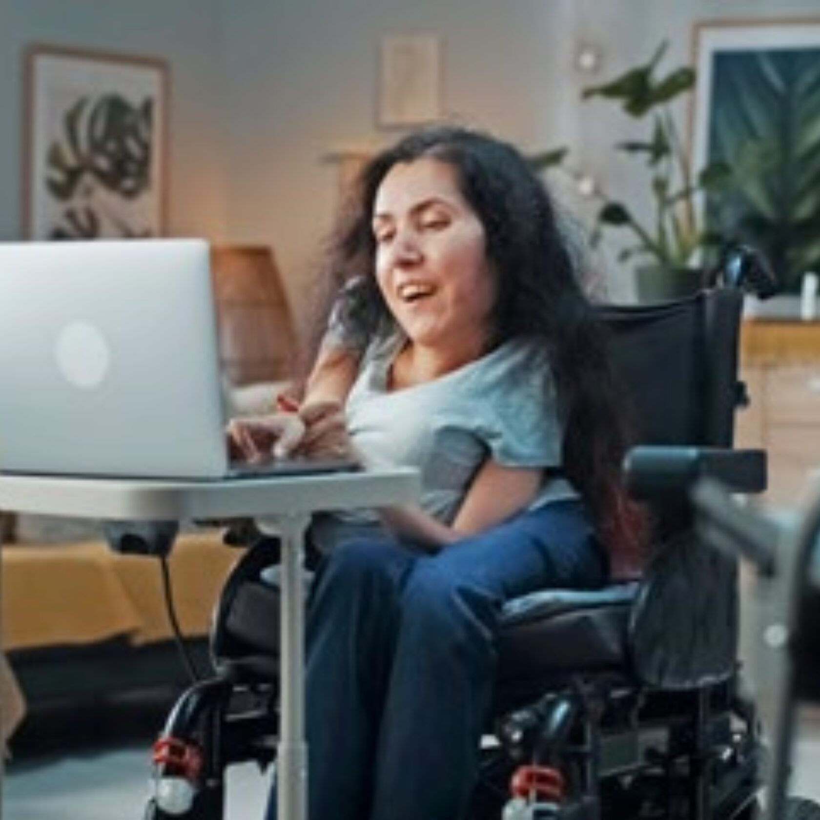 Kleinwüchsige Frau sitzt im Rollstuhl vor dem geöffneten Notebook