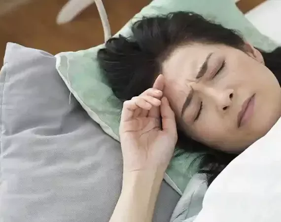 Eine Frau im Bett verzieht das Gesicht, weil es Morgen ist und sie schlecht geschlafen hat.