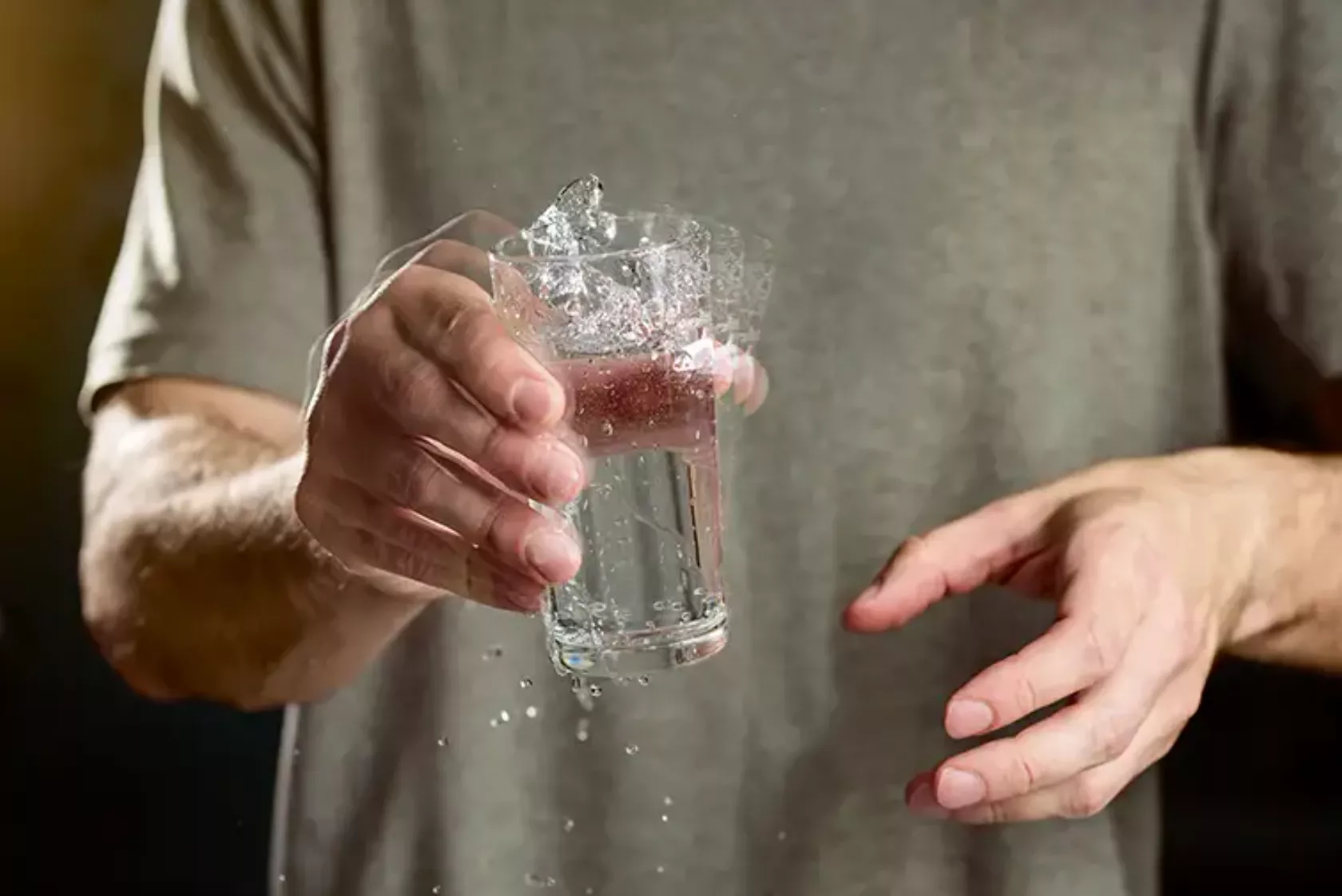 Nahaufnahme zitternde Hand hält ein Glas Wasser und verschüttet es.