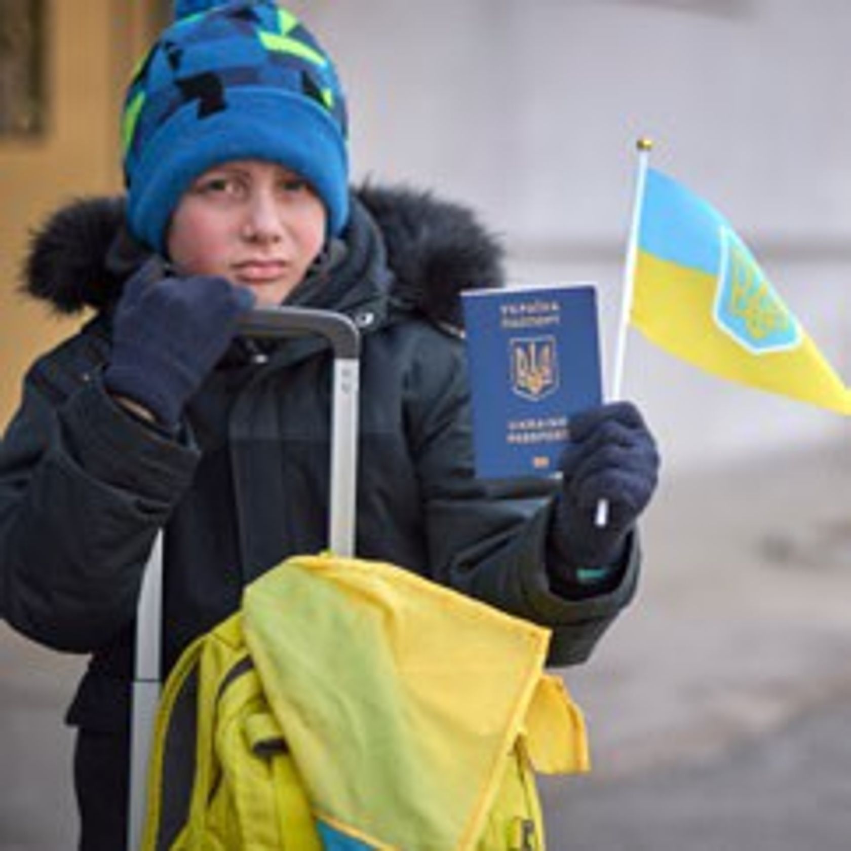 Ein Junge in Winterjacke hält seinen Ukrainischen Pass und eine ukrainische Flagge hoch.