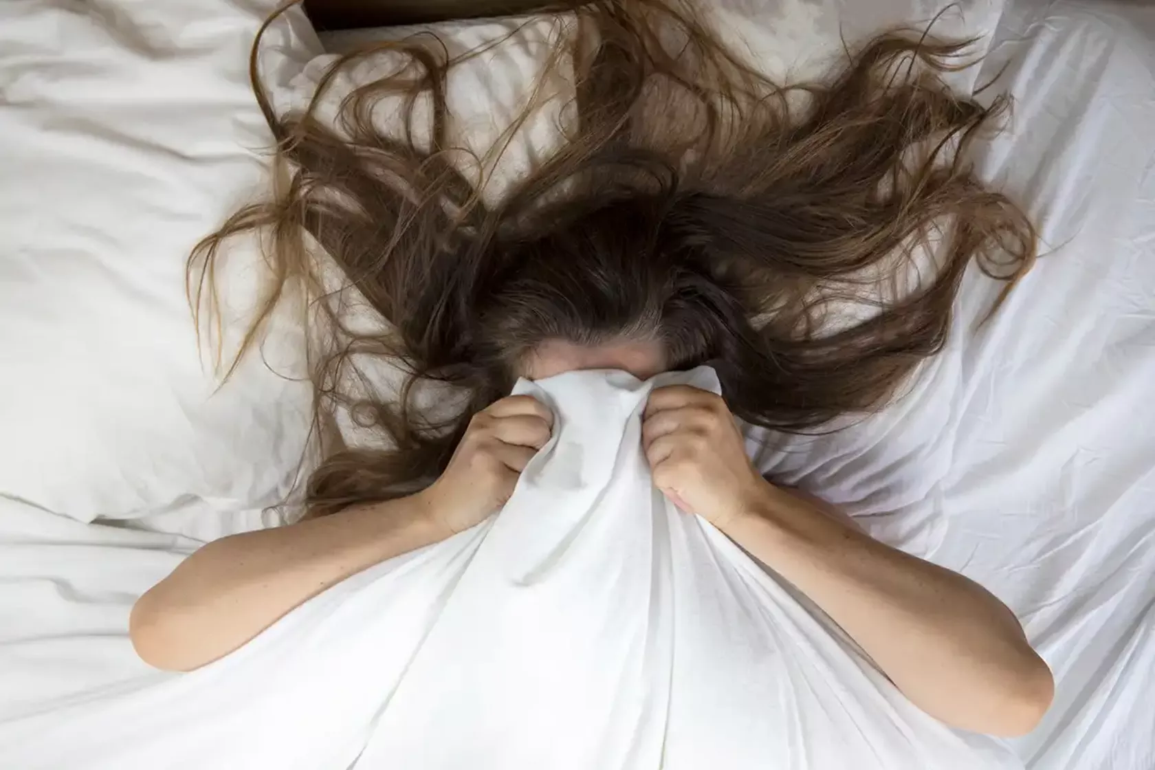 Frau zieht sich im Bett die Decke übers Gesicht.