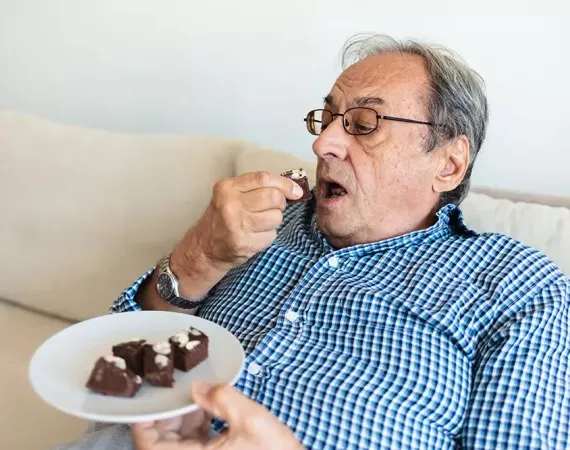 Senior sitzt auf dem Sofa und schaufelt Kuchen in sich hinein.