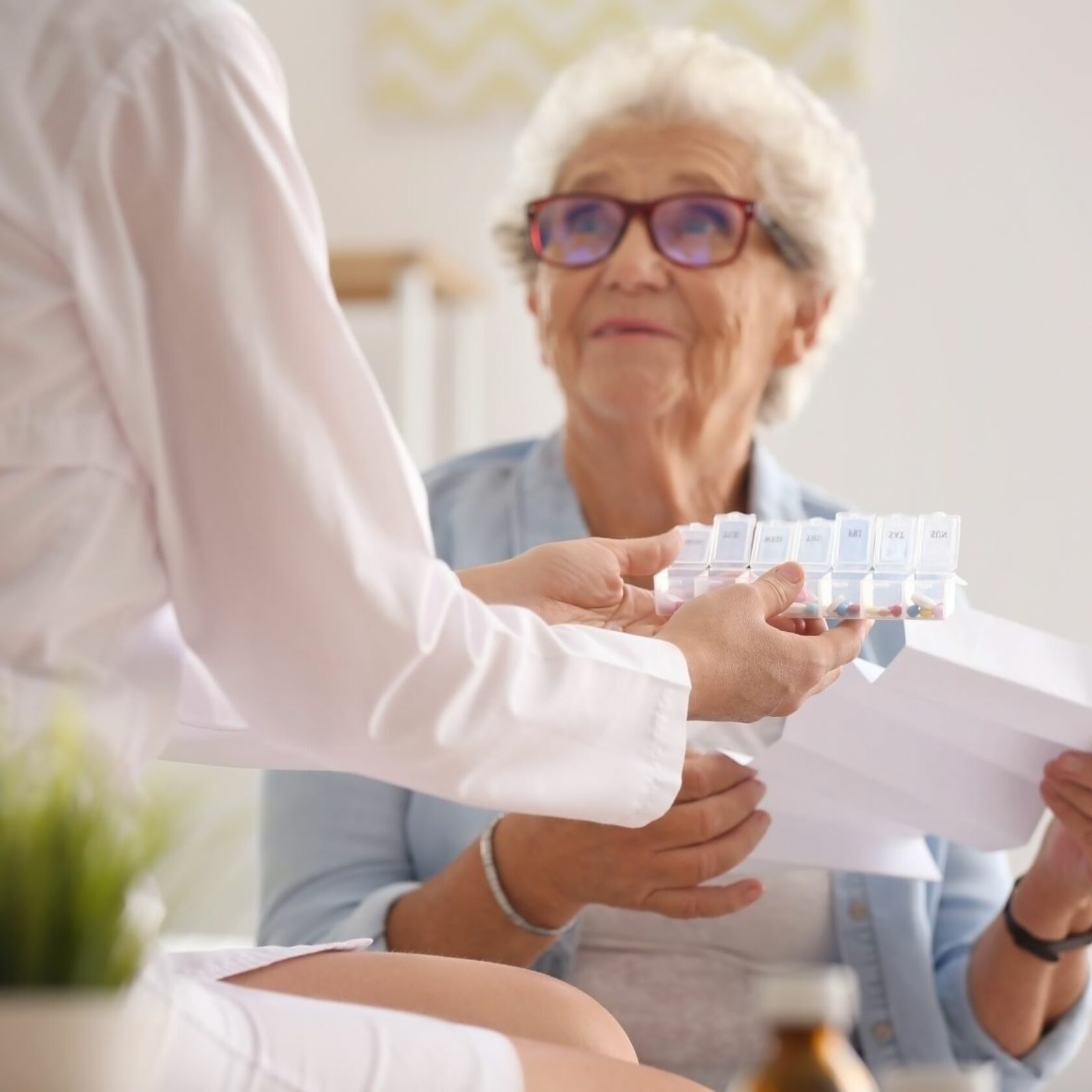 Seniorin blickt einer Pflegekraft entgegen die ihr Medikamente hinhält