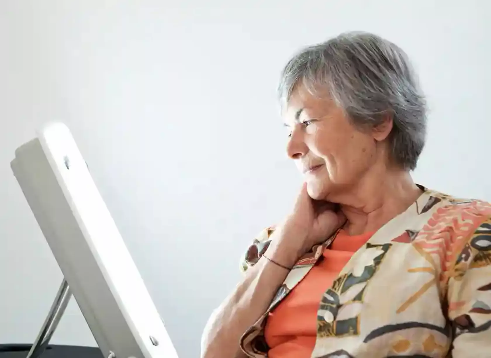 Ältere Frau sitzt neben einer Therapie-Lampe zur Tageslichttherapie.