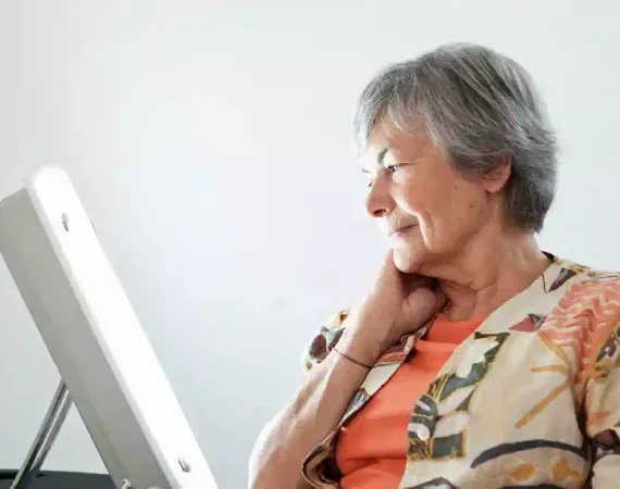 Ältere Frau sitzt neben einer Therapie-Lampe zur Tageslichttherapie.